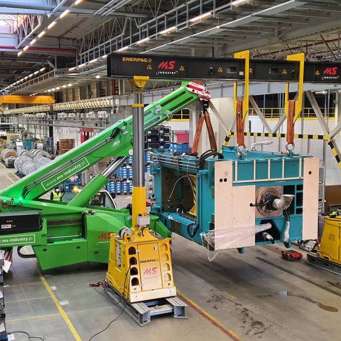 Precyzyjne pozycjonowanie korpusu prasy nad naczepa transportowa w hali produkcyjnej. 